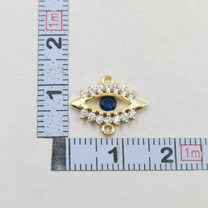 Detailed view of evil eye pendant with blue gemstone and cubic zirconia beside a ruler