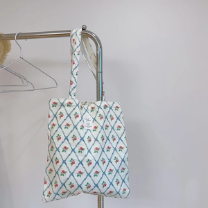 Detail of floral tote bag with blue grid pattern and small roses on a metal hanger