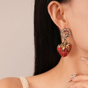 Detail of strawberry drop earring with red crystals and vintage gold logo on model