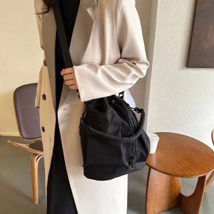Vue détaillée d'un sac seau noir en nylon porté en bandoulière avec un manteau beige