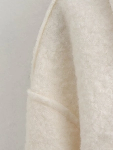 Close-up of white bouclé wool fabric texture and stitching detail on the outerwear jacket