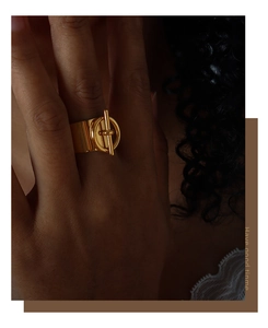 Detalle de un anillo ancho dorado con cierre OT mostrado en el dedo índice de una modelo