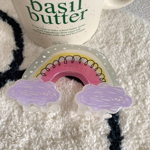 Detail of cute rainbow cloud acrylic hair claw clip on plush cream rug with a cup
