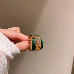 Close-up of irregular green enamel C-shaped gold metal earrings held in hand for scale