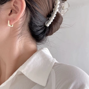 Side view of woman wearing elegant gold geometric earrings and a pearl hair claw clip
