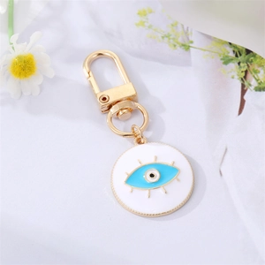 Détail du porte-clés œil bleu avec émail et cils dorés sur fond de texture blanche