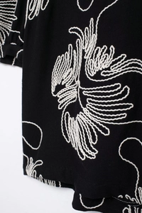 Close-up of white embroidery on black fabric showing textured leaf patterns