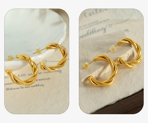 Detail view of gold twisted weave C-shape earrings on elegant white porcelain background
