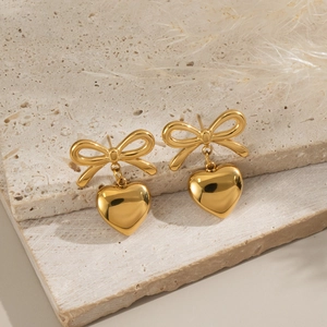 Detail of gold bow earrings with heart pendant on stone texture and feather decor