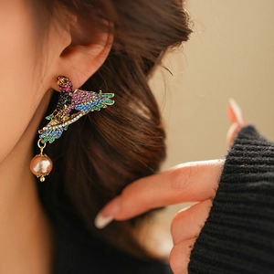 Close-up of vintage style bird earring with colorful rhinestones and champagne pearl drop
