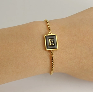 Close-up of gold plated adjustable bracelet with black rectangular letter E pendant