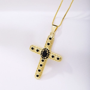 Detail of a gold cross necklace with intricate engravings and black gemstone inlays on silk