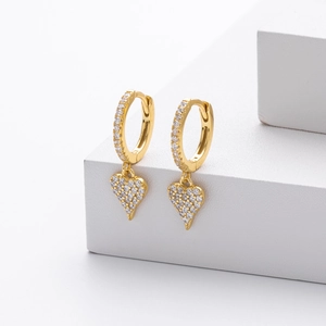 Close-up of golden heart earrings with sparkling white zircons on a white stone base