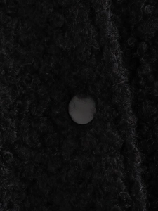 Macro shot of black fuzzy fleece texture and a smooth round button on the stylish jacket