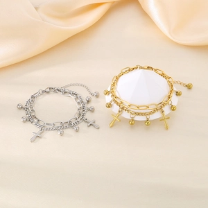 Detail of layered gold and silver cross charm bracelets on elegant silk background