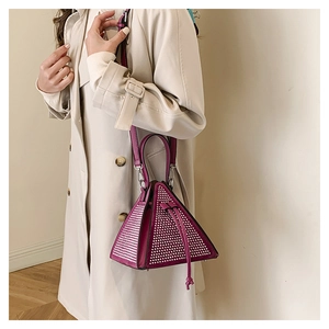Detail of magenta triangle bag with silver studs worn with a beige trench coat