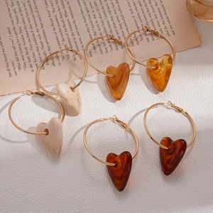 Six pairs of gold hoop earrings with acrylic heart pendants on vintage paper backdrop