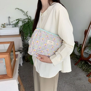 Floral makeup pouch held by model in a cozy indoor setting featuring a woven label detail