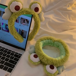 Set fascia e elastico rana in peluche verde per lavaggio viso su letto bianco