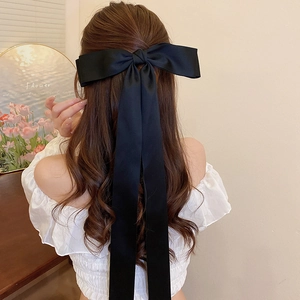 Detail view of a large black satin mesh bow hair clip with pearls on a model's hair