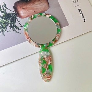 Detail view of green and brown tortoiseshell handheld mirror on a white surface with magazine