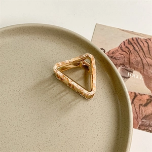 Close-up of triangle acetate hair claw with marble pattern and gold metal frame on a dish