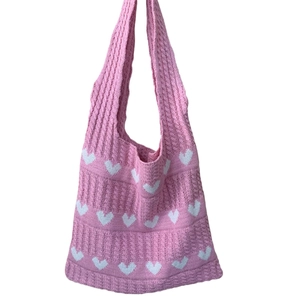 Detail of pink knitted tote bag featuring a white heart pattern and woven handle