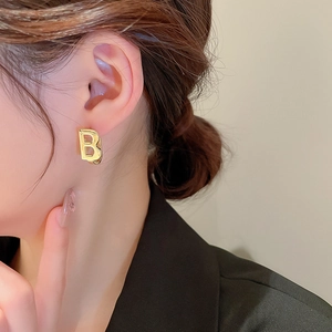 Close-up of a glossy gold metal letter B earring worn by a model in a modern style