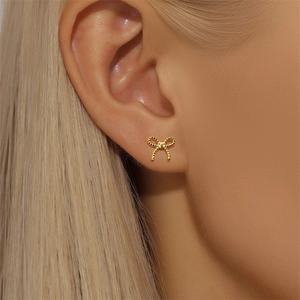 Gros plan d'une boucle d'oreille dorée en forme de nœud avec texture perlée