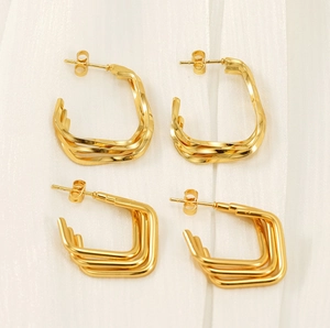 Dettaglio di orecchini a onde e quadrati placcati in oro 18K su tessuto bianco