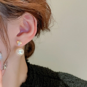 Detail of gold-plated zircon and large white pearl earrings worn by a model