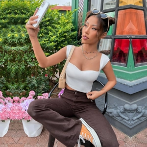 Outdoor lifestyle shot of a woman in a white ribbed crop top and brown wide-leg pants