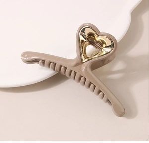 Detail of khaki shark hair claw with gold heart motif on a white ceramic tray