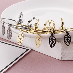 Hollow leaf pendant earrings in gold, silver and black on white ceramic display