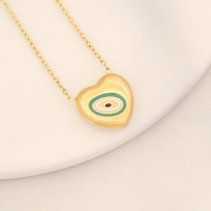 Close-up of golden heart-shaped necklace with green evil eye enamel on ceramic plate