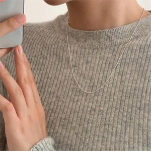 Close-up of a delicate 925 silver beaded necklace worn by a model on a grey sweater