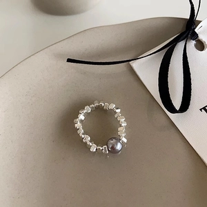 Detail of silver beaded ring with dark gray pearl on a minimalist beige ceramic plate