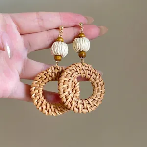 Detailed view of bohemian woven raffia earrings with gold studs and wooden bead accents