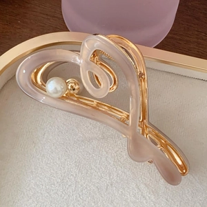 Detail of heart-shaped metal claw clip with beige resin and elegant pearl accent