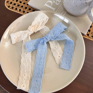 Detailed embroidery on lace bow hair clips in beige and blue resting on a ceramic plate