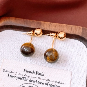 Detail of 18k gold plated drop earrings with tiger eye stone beads on a wooden tray
