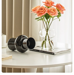 Detail of elegant clear glass and black ceramic vases with orange roses for home decor