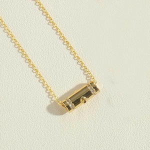 Close-up of golden cylinder pendant with rhinestone details and a delicate cable chain
