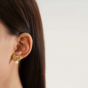 Elegant gold bow earrings with two round pearls shown on ear in a minimalist aesthetic