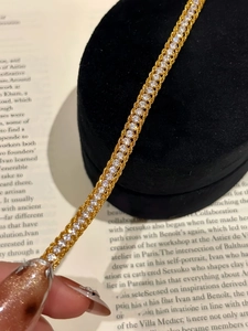 Macro detail of a woven gold snake tennis bracelet with sparkling zircons on velvet