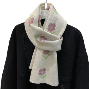 Cream knit scarf with pink floral patterns on a black coat backdrop for winter style