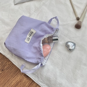 Close-up of lilac drawstring pouch storage bag with cosmetics on soft white fabric