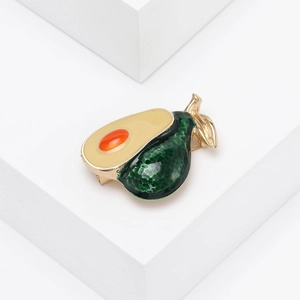 Close-up of cute avocado brooch with green enamel and orange stone on white stand