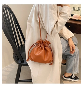 Braune weiche Eimertasche aus Leder mit Kordelzug getragen zu einem beigen Trenchcoat