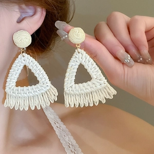 Détail des boucles d'oreilles bohèmes en raphia tissé avec de jolies franges crème